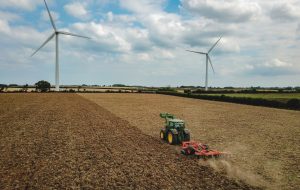 Tractor ploughing through fields with air turbines in the background.