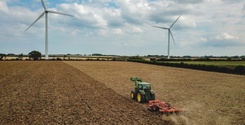 Tractor ploughing through fields with air turbines in the background.