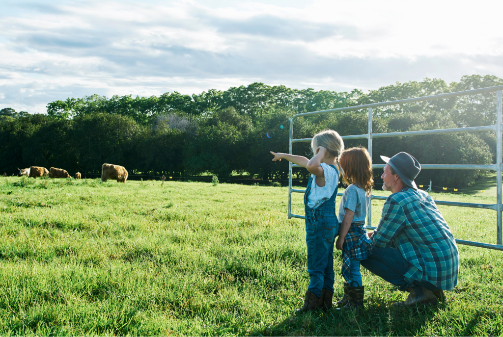 Farmer looking at cows in  field with two small children. Represents the future of farming. 